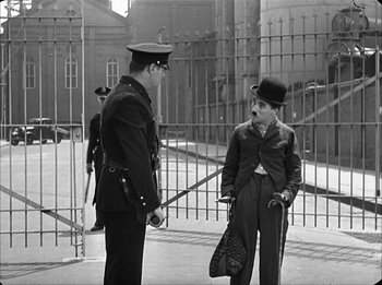Movie still from “Modern Times” (1936), directed by Charles Chaplin – A man in a top hat talking to another man in a uniform; Wide shot, Over the shoulder angle