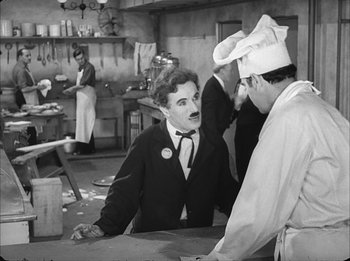 Movie still from “Modern Times” (1936), directed by Charles Chaplin – A group of people standing around in a kitchen; Medium shot, Over the shoulder angle