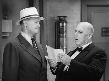 Movie still from “Modern Times” (1936), directed by Charles Chaplin – Two men in suits and hats are looking at a piece of paper; Medium shot, Over the shoulder angle