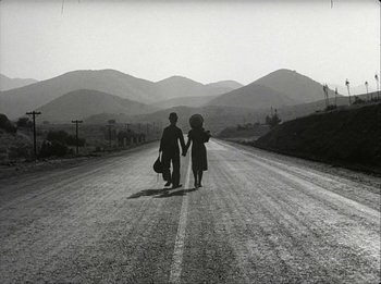 Movie still from “Modern Times” (1936), directed by Charles Chaplin – A man and a woman walking down the middle of a road; Wide shot, High angle
