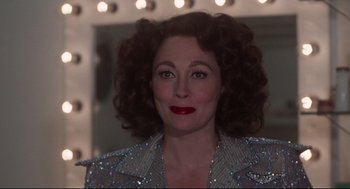 Movie still from “Mommie Dearest” (1981), directed by Frank Perry – A person with curly hair wearing a jacket; Close Up shot, Over the shoulder angle