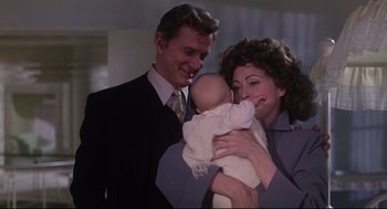 Movie still from “Mommie Dearest” (1981), directed by Frank Perry – A man and a woman holding a baby in her arms; Medium shot, Over the shoulder angle