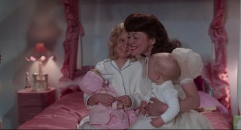 Movie still from “Mommie Dearest” (1981), directed by Frank Perry – A woman and two young girls are holding a doll; Medium shot, High angle