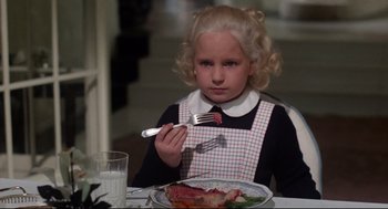 Movie still from “Mommie Dearest” (1981), directed by Frank Perry – A little girl sitting at a table with a plate of food; Medium shot, High angle
