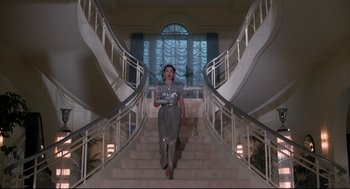 Movie still from “Mommie Dearest” (1981), directed by Frank Perry – A woman walking down a set of stairs in front of a window; Wide shot, Low angle