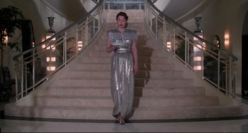 Movie still from “Mommie Dearest” (1981), directed by Frank Perry – A woman in a silver dress walking down a set of stairs; Wide shot, Low angle