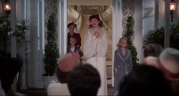 Movie still from “Mommie Dearest” (1981), directed by Frank Perry – A group of people standing in front of a staircase; Medium shot, Over the shoulder angle