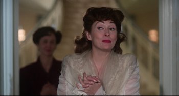 Movie still from “Mommie Dearest” (1981), directed by Frank Perry – An older woman in a white dress clasps her hands; Close Up shot, Low angle