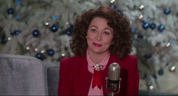 Movie still from “Mommie Dearest” (1981), directed by Frank Perry – A woman in a red jacket is sitting in front of a microphone; Close Up shot, Over the shoulder angle