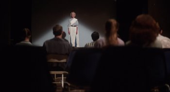 Movie still from “Mommie Dearest” (1981), directed by Frank Perry – A woman standing in front of an audience in front of a screen; Wide shot, Over the shoulder angle