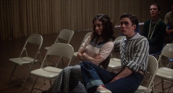 Movie still from “Mommie Dearest” (1981), directed by Frank Perry – A man and a woman sitting next to each other in front of white folding chairs; Medium shot, Over the shoulder angle