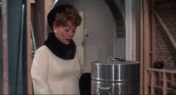Movie still from “Mommie Dearest” (1981), directed by Frank Perry – A woman in a white dress and a black hat is next to a metal container; Medium shot, Low angle
