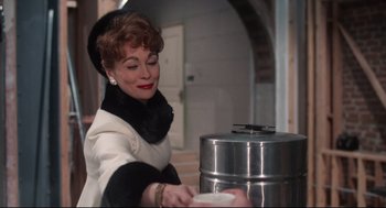 Movie still from “Mommie Dearest” (1981), directed by Frank Perry – An older woman in a black and white outfit is putting something in a metal container; Medium shot, Low angle