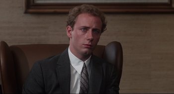 Movie still from “Mommie Dearest” (1981), directed by Frank Perry – A man in a suit and tie sitting in a chair; Close Up shot, Over the shoulder angle