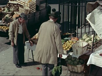 Movie still from “My Uncle” (1958), directed by Jacques Tati – Two men standing in front of a table of fruits and vegetables; Wide shot, High angle
