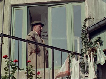 Movie still from “My Uncle” (1958), directed by Jacques Tati – An older man smoking a pipe while standing on a balcony; Medium shot, Low angle