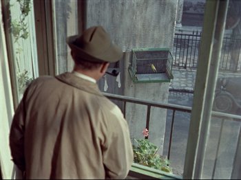 Movie still from “My Uncle” (1958), directed by Jacques Tati – A man looking out of a window at a bird in a cage; Wide shot, High angle