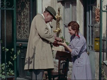 Movie still from “My Uncle” (1958), directed by Jacques Tati – An older man and a young woman holding a piece of food; Medium shot, High angle