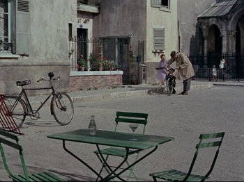 Movie still from “My Uncle” (1958), directed by Jacques Tati – Two people sitting at a table in the middle of a street; Extreme Wide shot, High angle
