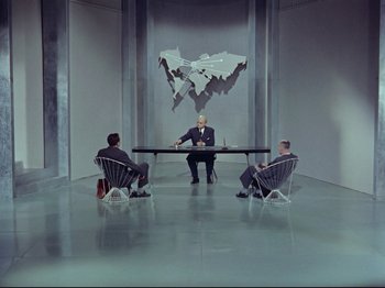 Movie still from “My Uncle” (1958), directed by Jacques Tati – Three men sitting at a table in front of a map; Extreme Wide shot, High angle