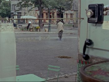 Movie still from “My Uncle” (1958), directed by Jacques Tati – A man riding a bike down a street; Wide shot, High angle