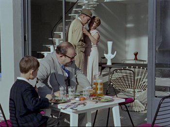 Movie still from “My Uncle” (1958), directed by Jacques Tati – A man and a woman sitting at a table with a child; Wide shot, High angle