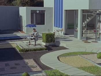 Movie still from “My Uncle” (1958), directed by Jacques Tati – A man sitting on a chair in the middle of a garden; Extreme Wide shot, High angle