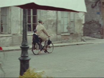 Movie still from “My Uncle” (1958), directed by Jacques Tati – A man riding a bike with a child on the back; Wide shot, High angle