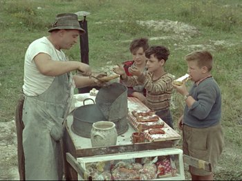 Movie still from “My Uncle” (1958), directed by Jacques Tati – An old photo of a man and some kids at an outdoor food stand; Medium shot, High angle