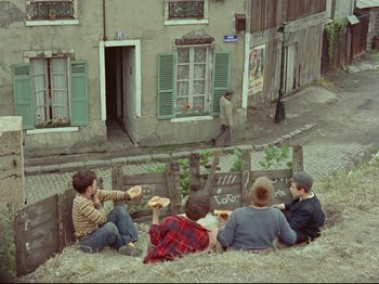 Movie still from “My Uncle” (1958), directed by Jacques Tati – A group of people sitting on the side of a road; Wide shot, High angle