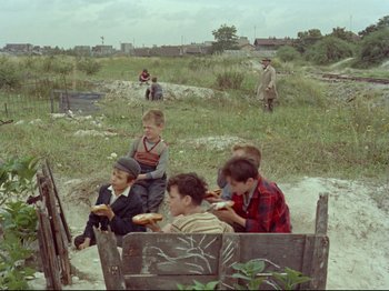 Movie still from “My Uncle” (1958), directed by Jacques Tati – A group of children sitting in a field eating food; Wide shot, High angle