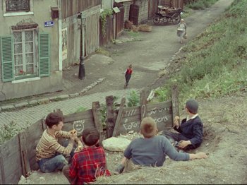 Movie still from “My Uncle” (1958), directed by Jacques Tati – A group of young men sitting on the side of a road; Extreme Wide shot, High angle