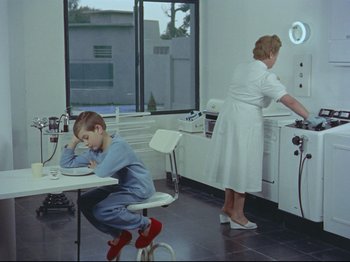 Movie still from “My Uncle” (1958), directed by Jacques Tati – A boy sitting on a chair in a room with an older woman; Wide shot, High angle