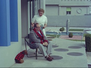 Movie still from “My Uncle” (1958), directed by Jacques Tati – An older man sitting in a chair next to an older woman; Wide shot, High angle