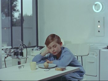 Movie still from “My Uncle” (1958), directed by Jacques Tati – A boy sitting at a table with a plate of food in front of him; Medium shot, High angle
