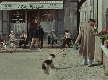 Movie still from “My Uncle” (1958), directed by Jacques Tati – A man walking a dog down a street; Wide shot, High angle