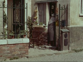 Movie still from “My Uncle” (1958), directed by Jacques Tati – An older woman standing in front of an open door; Wide shot, High angle