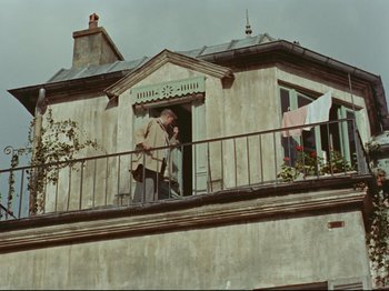Movie still from “My Uncle” (1958), directed by Jacques Tati – An older man standing on a balcony with a guitar; Wide shot, Low angle