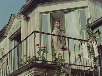 Movie still from “My Uncle” (1958), directed by Jacques Tati – A man standing on a balcony looking out of the window; Wide shot, Low angle