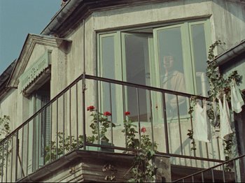 Movie still from “My Uncle” (1958), directed by Jacques Tati – An older woman sitting on the balcony of a house; Wide shot, Low angle