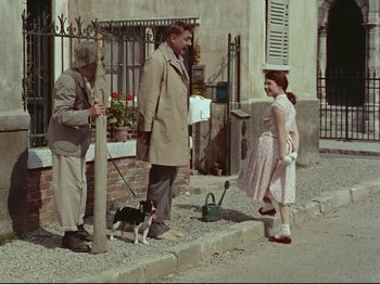 Movie still from “My Uncle” (1958), directed by Jacques Tati – A man and a woman standing next to each other on the sidewalk; Wide shot, Over the shoulder angle