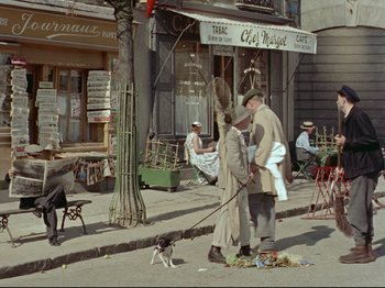 Movie still from “My Uncle” (1958), directed by Jacques Tati – Two men and a dog on the sidewalk of a street; Wide shot, High angle