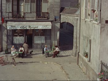 Movie still from “My Uncle” (1958), directed by Jacques Tati – A group of people sitting on benches in front of a building; Extreme Wide shot, High angle