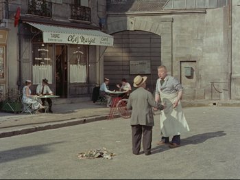 Movie still from “My Uncle” (1958), directed by Jacques Tati – Two men standing on the sidewalk in front of a restaurant; Wide shot, High angle