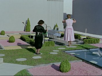 Movie still from “My Uncle” (1958), directed by Jacques Tati – Two women in dresses are standing in a garden; Extreme Wide shot, High angle