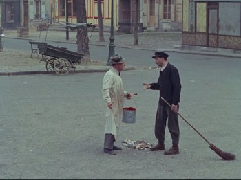 Movie still from “My Uncle” (1958), directed by Jacques Tati – Two men are standing on the street and one of them is holding a paint brush; Wide shot, High angle