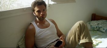 Movie still from “Monday” (2020), directed by Argyris Papadimitropoulos – A man sitting on a couch holding a cell phone; Medium shot, High angle