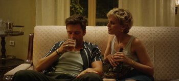 Movie still from “Monday” (2020), directed by Argyris Papadimitropoulos – A man and a woman sitting on a couch drinking beer; Medium shot, Over the shoulder angle