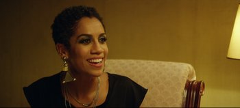 Movie still from “Monday” (2020), directed by Argyris Papadimitropoulos – A woman sitting on top of a couch smiling for the camera; Close Up shot, Over the shoulder angle