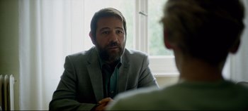 Movie still from “Monday” (2020), directed by Argyris Papadimitropoulos – A man sitting in front of another man in front of a window; Close Up shot, Over the shoulder angle